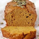 A loaf of sliced healthy pumpkin bread on a wooden board with autumn decorations.
