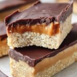 Layered peanut butter protein bars with a chocolate top on a wooden board