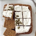 A sliced piece of moist pumpkin cake with creamy white frosting on a wooden board