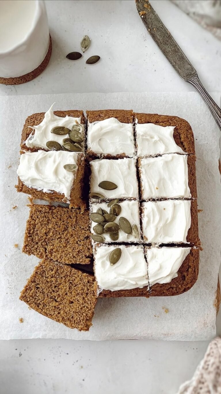 A sliced piece of moist pumpkin cake with creamy white frosting on a wooden board