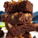 Dense fudgy flourless brownies topped with crushed salted pretzels in a baking pan