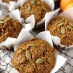 A stack of golden brown whole wheat pumpkin muffins on a wire cooling rack.
