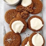 A plate of soft pumpkin cookies drizzled with white protein icing on a wooden table.