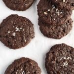 A pile of fudgy chocolate banana brownie cookies with melted chocolate chips on a wire rack.