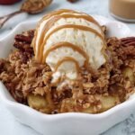A single serve ramekin filled with bubbly peanut butter apple crisp and a golden oat topping.