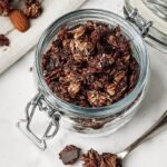 A close-up shot of crunchy dark chocolate almond granola on a baking sheet with dark chocolate chips.