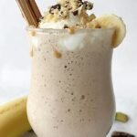 A thick chocolate protein shake in a glass topped with walnuts and chocolate chips