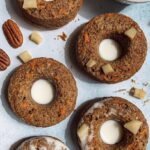 Six golden-brown baked carrot cake donuts on a wire cooling rack with a light cream cheese drizzle.