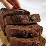 A sliced loaf of dark chocolate banana bread with melted chocolate chips on top.