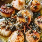 Golden brown pan-seared sea scallops drizzled with lemon butter sauce and fresh parsley on a white plate.