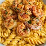 A white bowl filled with creamy Cajun shrimp pasta garnished with fresh parsley and bell peppers.