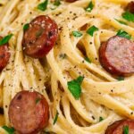 A skillet filled with creamy cajun sausage pasta, sliced andouille sausage, and colorful bell peppers.
