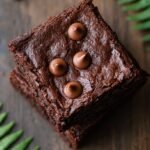 A stack of fudgy chocolate brownies topped with chocolate chips on a white plate.