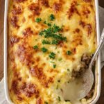 A bubbling ceramic dish of creamed cabbage and ground beef casserole with melted cheddar cheese on top.