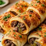 Close up of several roast beef roll ups filled with melted provolone cheese, green peppers, and onions on a baking sheet.