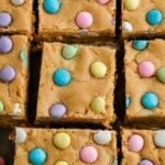 A close-up of chewy Easter cookie bars with pastel M&Ms and sprinkles in a baking pan.