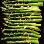 Fresh roasted asparagus spears on a baking sheet with lemon wedges.
