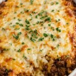 A 9x13 baking dish filled with French Onion Ground Beef and rice topped with melted Gruyère cheese and fresh parsley.