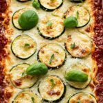 A bubbling dish of cheesy zucchini lasagna with golden brown mozzarella on top.