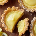 Twelve golden mini lemon pies with coconut tops in a muffin tin