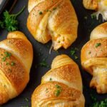 Golden brown crescent rolls filled with melted cheese and shredded chicken on a parchment-lined baking sheet.