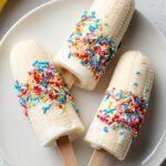 Four frozen banana yogurt pops coated in granola on a parchment-lined tray.