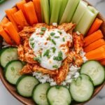 A white bowl filled with creamy cottage cheese, spicy buffalo chicken, fresh cucumbers, and cherry tomatoes.