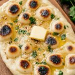 Soft and charred homemade naan bread brushed with butter and cilantro in a cast iron skillet