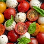 A platter of sliced mozzarella, ripe tomatoes, and fresh basil leaves drizzled with balsamic glaze.