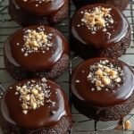 Golden brown chocolate hazelnut cookies dipped halfway in dark chocolate ganache on a parchment lined tray.