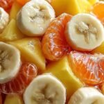 A vibrant yellow gelatin salad with bits of pineapple and shredded carrots served in squares on a white plate.