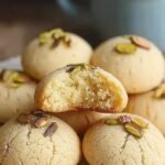 Golden Indian Nankhatai cookies topped with green pistachios on a baking sheet