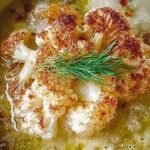 A bowl of smooth white cauliflower soup topped with golden roasted florets and fresh chives.