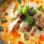 A bowl of creamy orange buffalo chicken soup topped with shredded cheese and diced celery