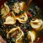 A steaming bowl of dumpling soup with green onions and chili oil drizzle