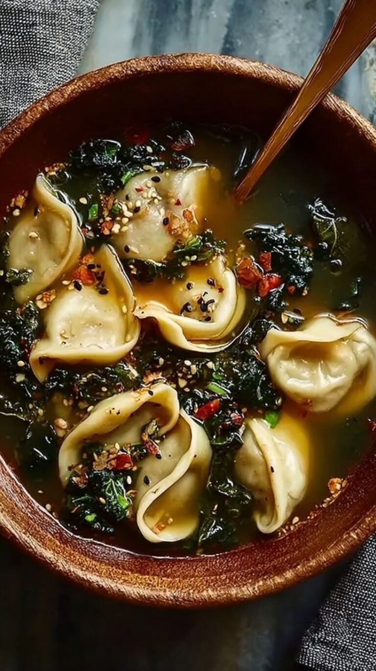 A steaming bowl of dumpling soup with green onions and chili oil drizzle