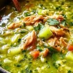 A large bowl of vibrant green Peruvian chicken soup with rice, potatoes, and peas.