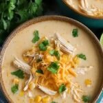 A bowl of creamy white chicken chili topped with cilantro, cheese, and lime wedges
