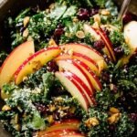 A large bowl of shredded kale salad topped with thin apple slices, almonds, and shaved parmesan cheese.