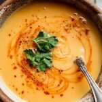 A bowl of creamy Turkish red lentil soup drizzled with red chili butter and served with lemon wedges.