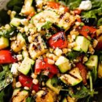 A colorful bowl of grilled zucchini salad with charred corn, sweet peppers, and feta cheese