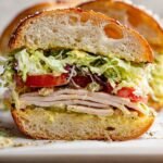 A toasted Italian grinder sandwich piled high with a creamy shredded lettuce salad and melted cheese.