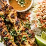 Grilled chicken skewers on a platter with a bowl of peanut dipping sauce
