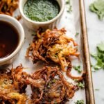 A platter of golden brown, crispy Indian vegetable pakoras served with green chutney.