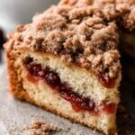 A square slice of cranberry sauce coffee cake with a thick layer of red berries and golden streusel topping on a white plate.