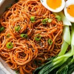A bowl of glossy Sesame Gochujang Noodles topped with green onions and sesame seeds