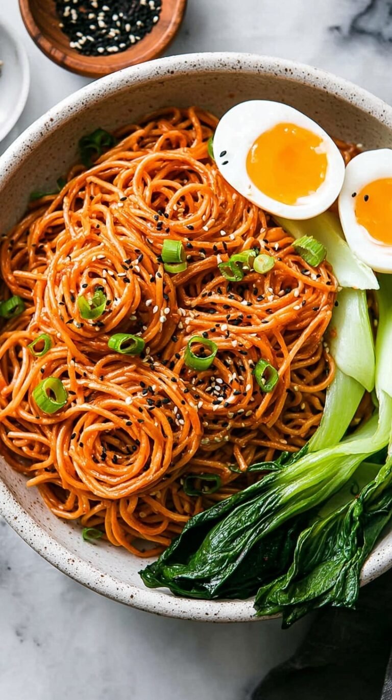 A bowl of glossy Sesame Gochujang Noodles topped with green onions and sesame seeds
