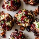 Small goat cheese balls coated in red cranberries and green chives on a white platter with honey drizzle