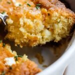 A golden brown Jiffy corn casserole in a white baking dish with melted cheddar cheese on top.