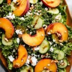A fresh sweet peach salad with mixed greens, goat cheese crumbles, and toasted pecans on a white plate.